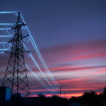 Electric transmission towers with glowing wires against the sunset sky background. High voltage electrical pylons. Energy concept.